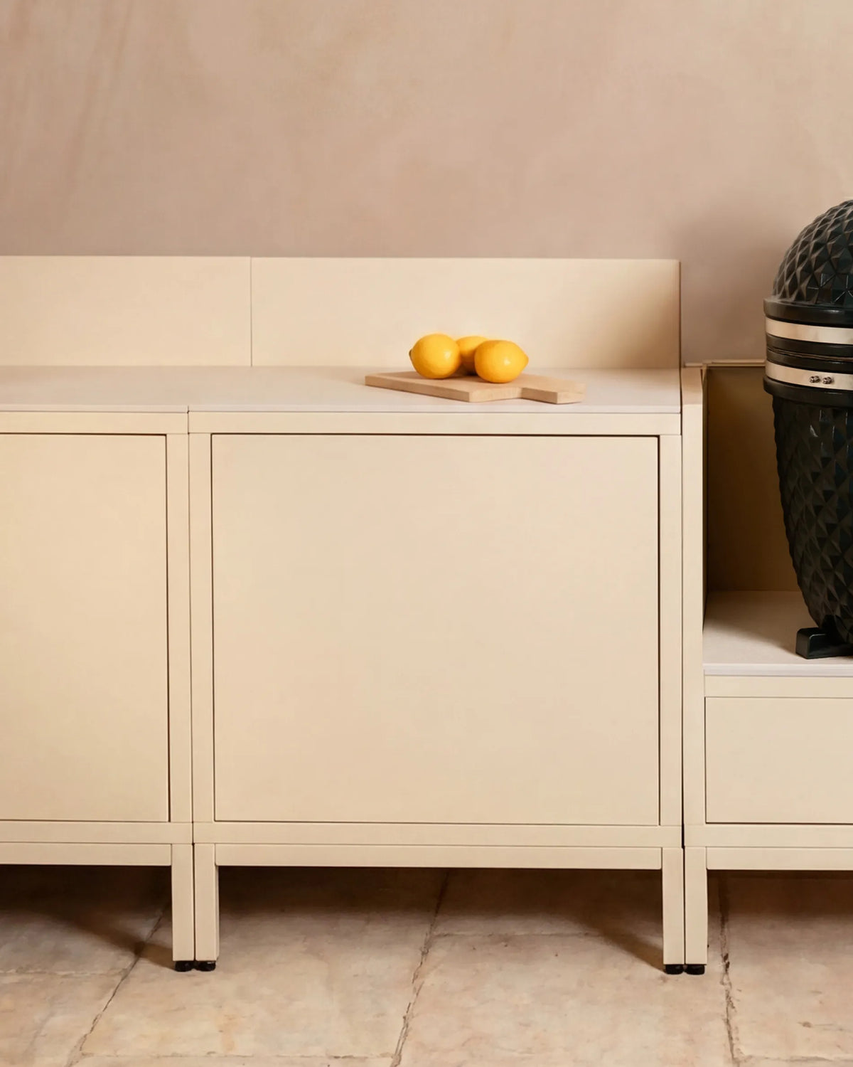 Módulos em bege creme Classic PILOTIS para cozinha exterior, com kamado e limões sobre a tábua