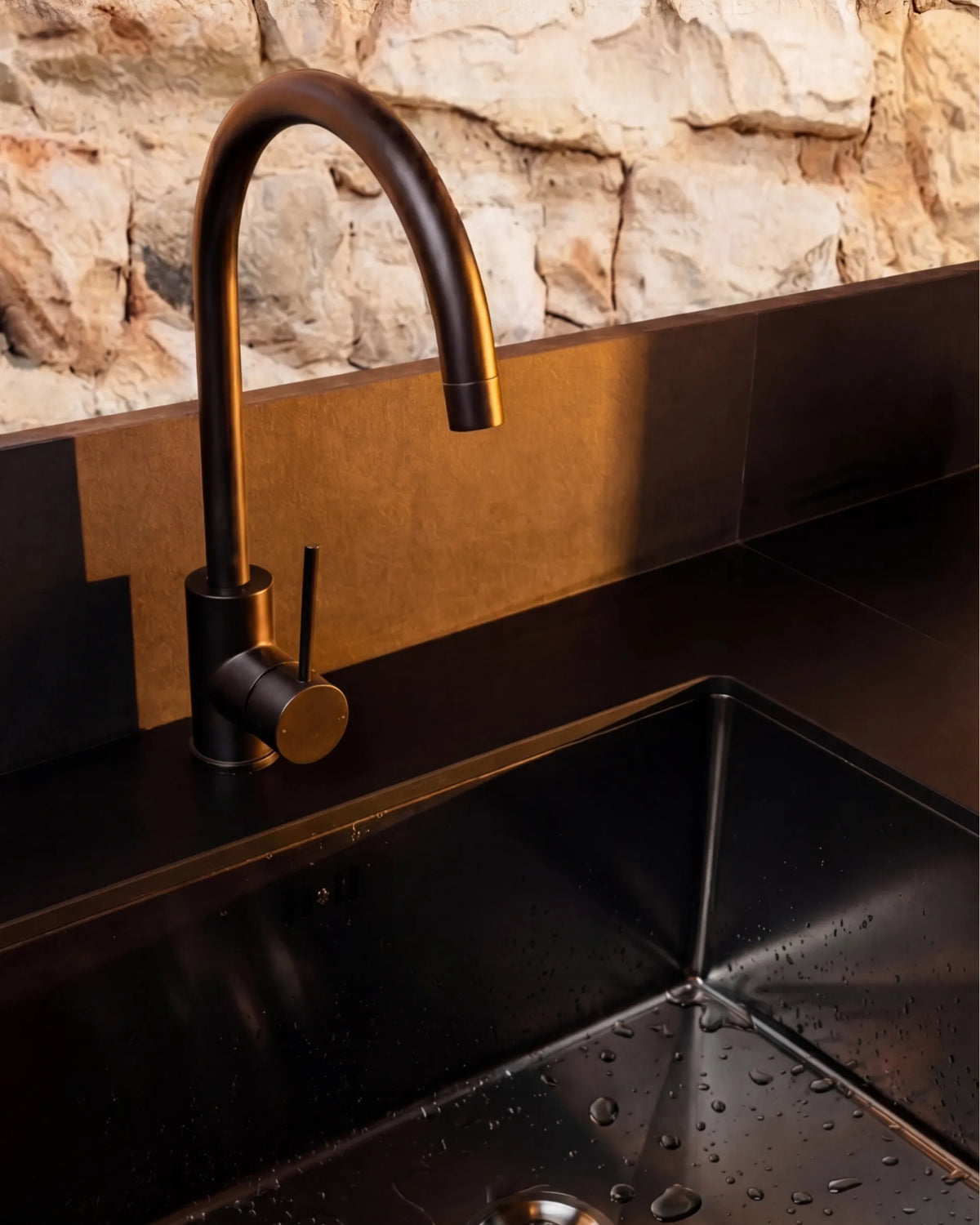 Lavatório preto e torneira com acabamento em bronze do módulo de lava-loiça PILOTIS, vista em detalhe