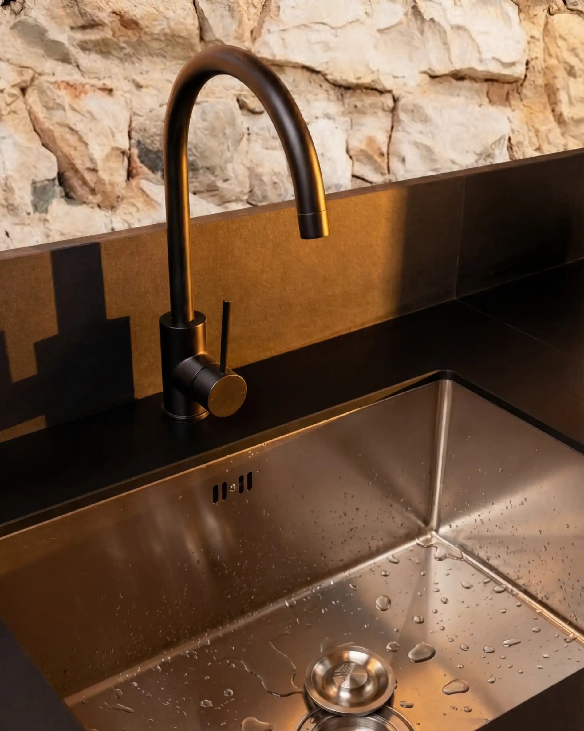 Detalhe de lava-loiça em inox com torneira preta na cozinha exterior Kokko