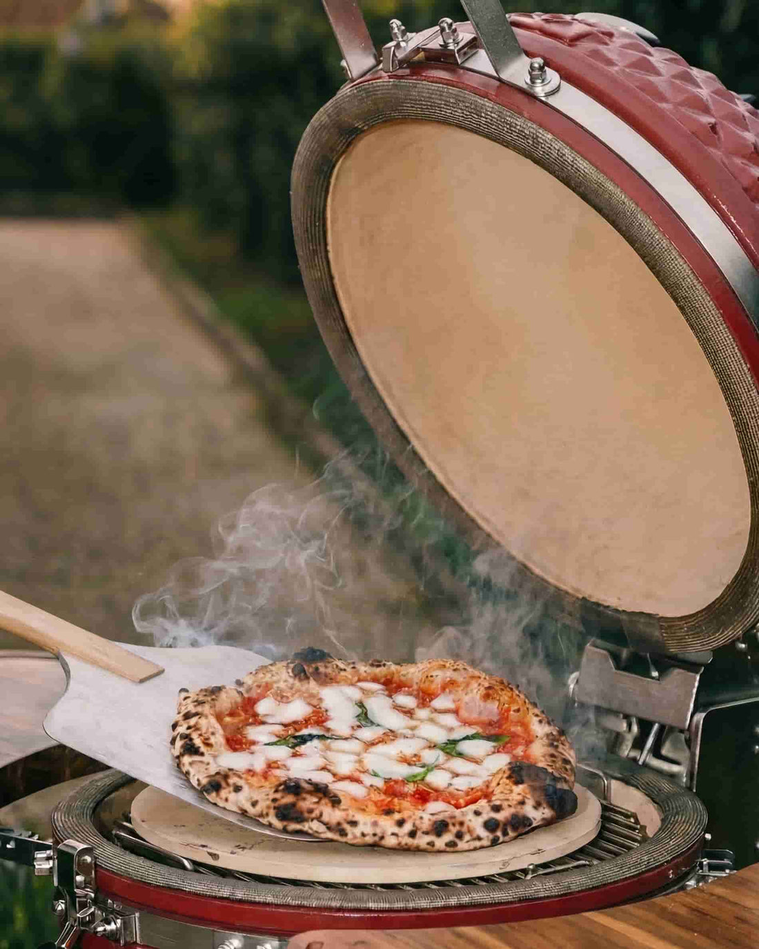 Pizza colocada numa pedra refratária dentro de um kamado Kokko aberto, a cozinhar com carvão vegetal.