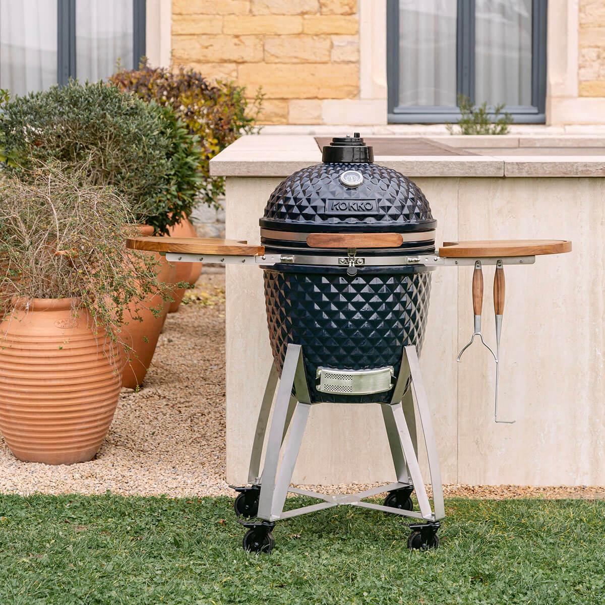 Kamado Kokko azul-marinho em cerâmica, equipado com prateleiras de madeira e suporte móvel com rodas.