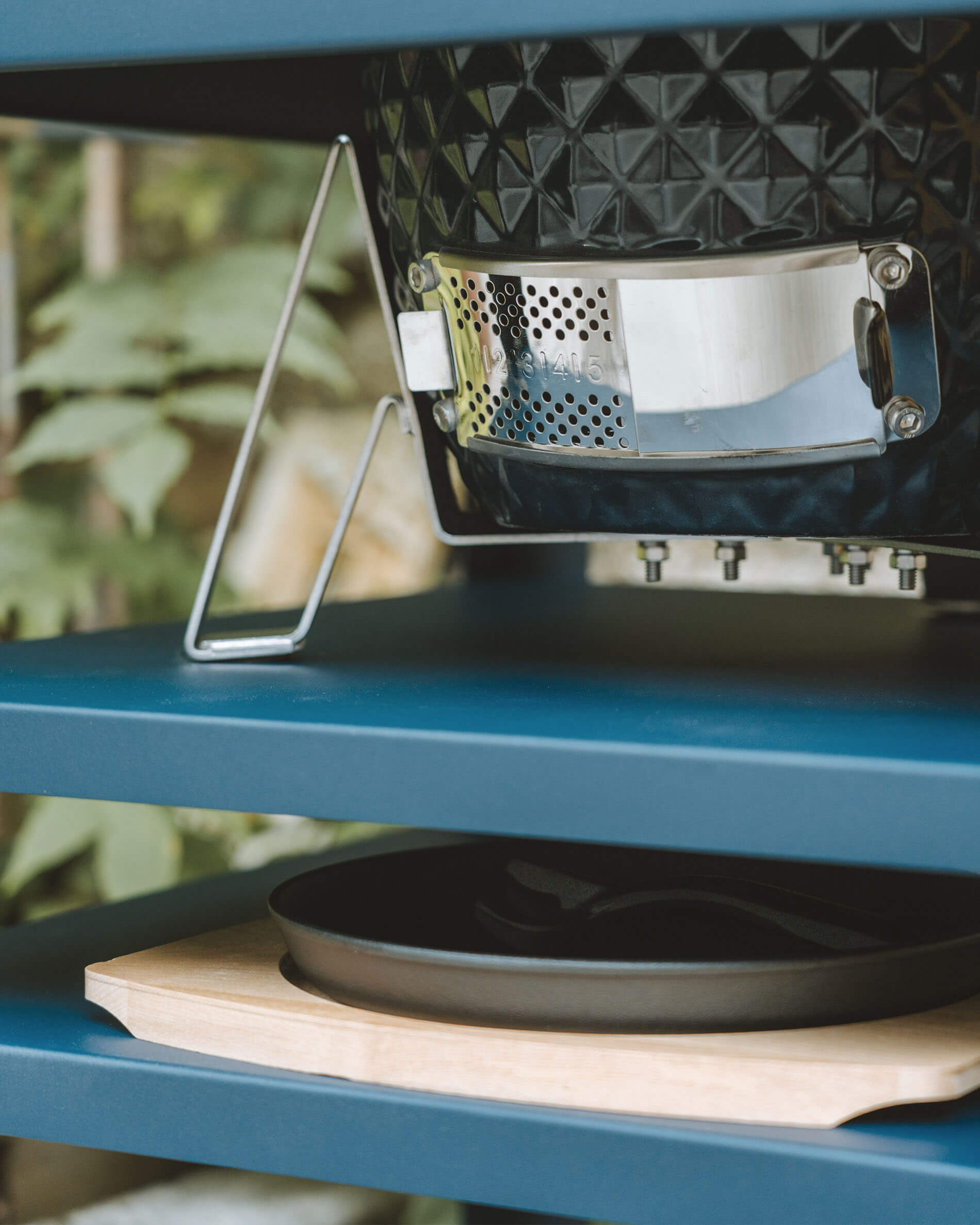 Vista aproximada da ventilação inferior em aço inoxidável de um kamado Kokko, integrada numa mesa metálica com gaveta para recolha de cinzas.