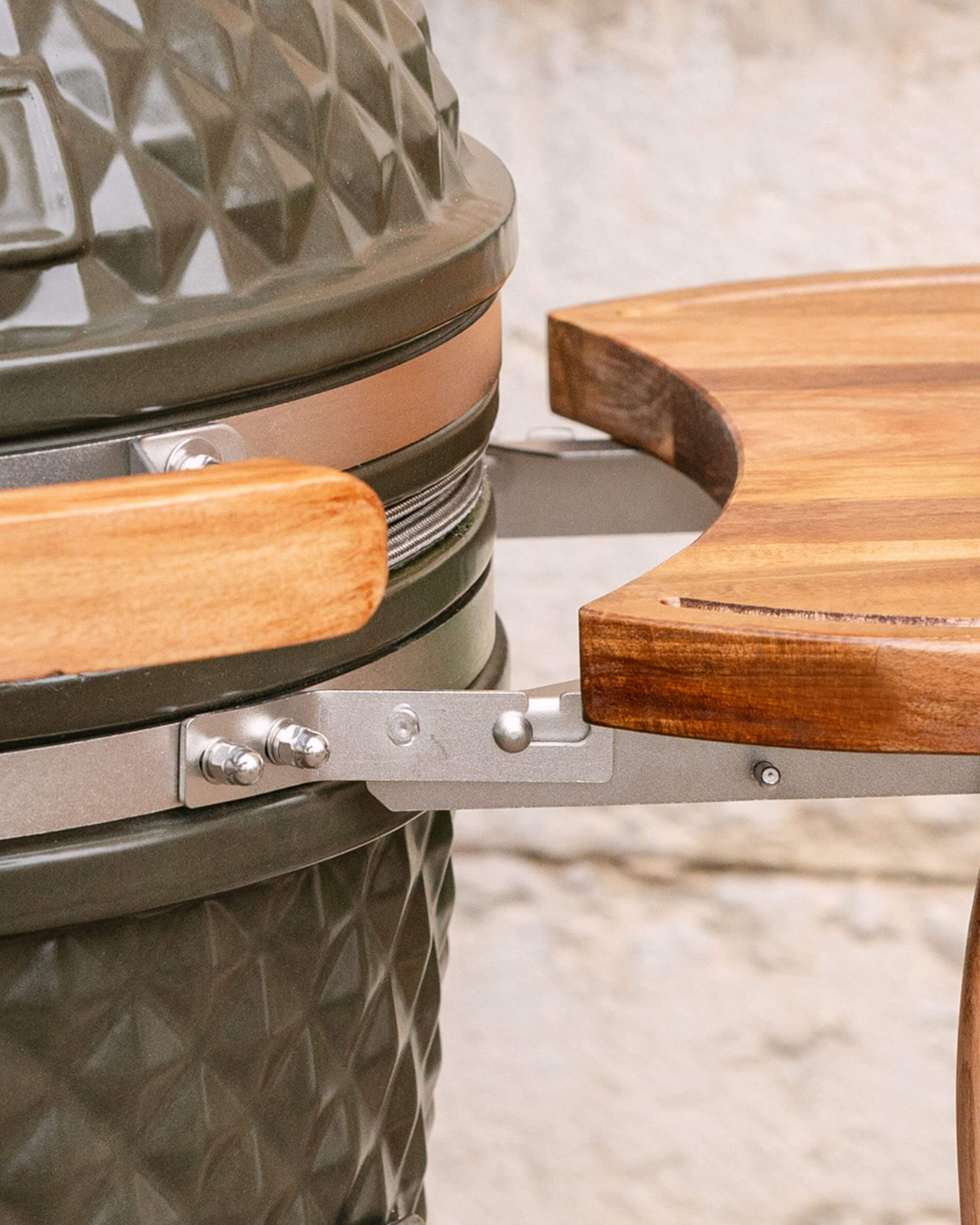 Close-up da fixação metálica que liga o tabuleiro lateral em madeira ao kamado, mostrando o sistema de encaixe e a parafusaria.