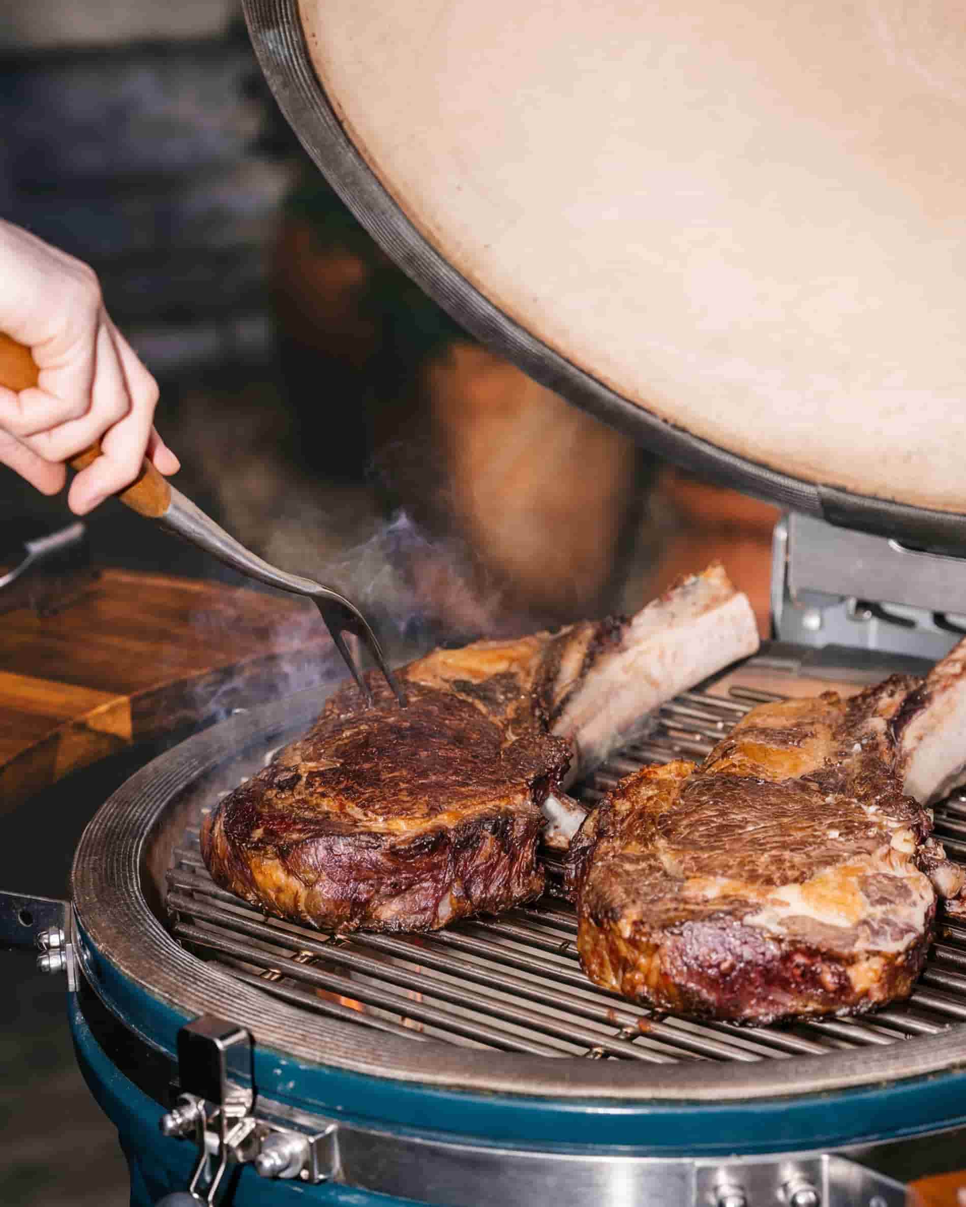 Grelhar carne na grelha de um kamado Kokko XL 22 polegadas, com a tampa aberta.