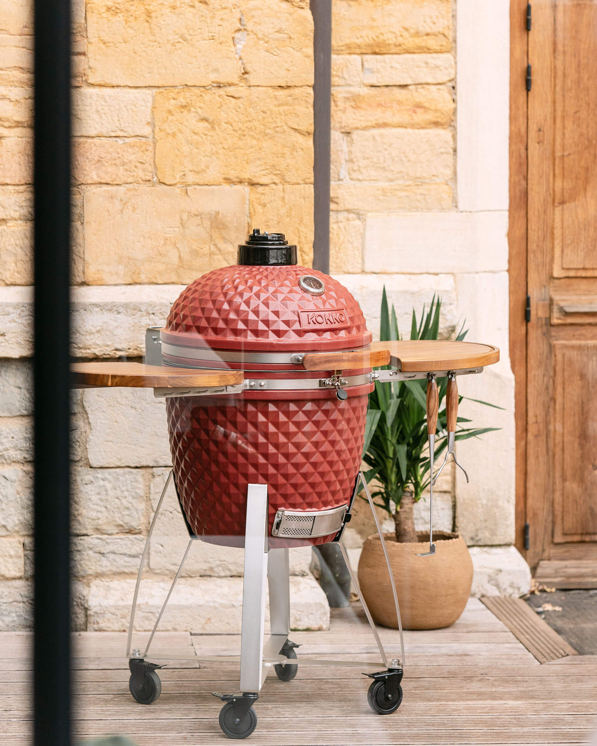Kamado Kokko XL 22 polegadas em cerâmica vermelho óxido instalado num carrinho no exterior.