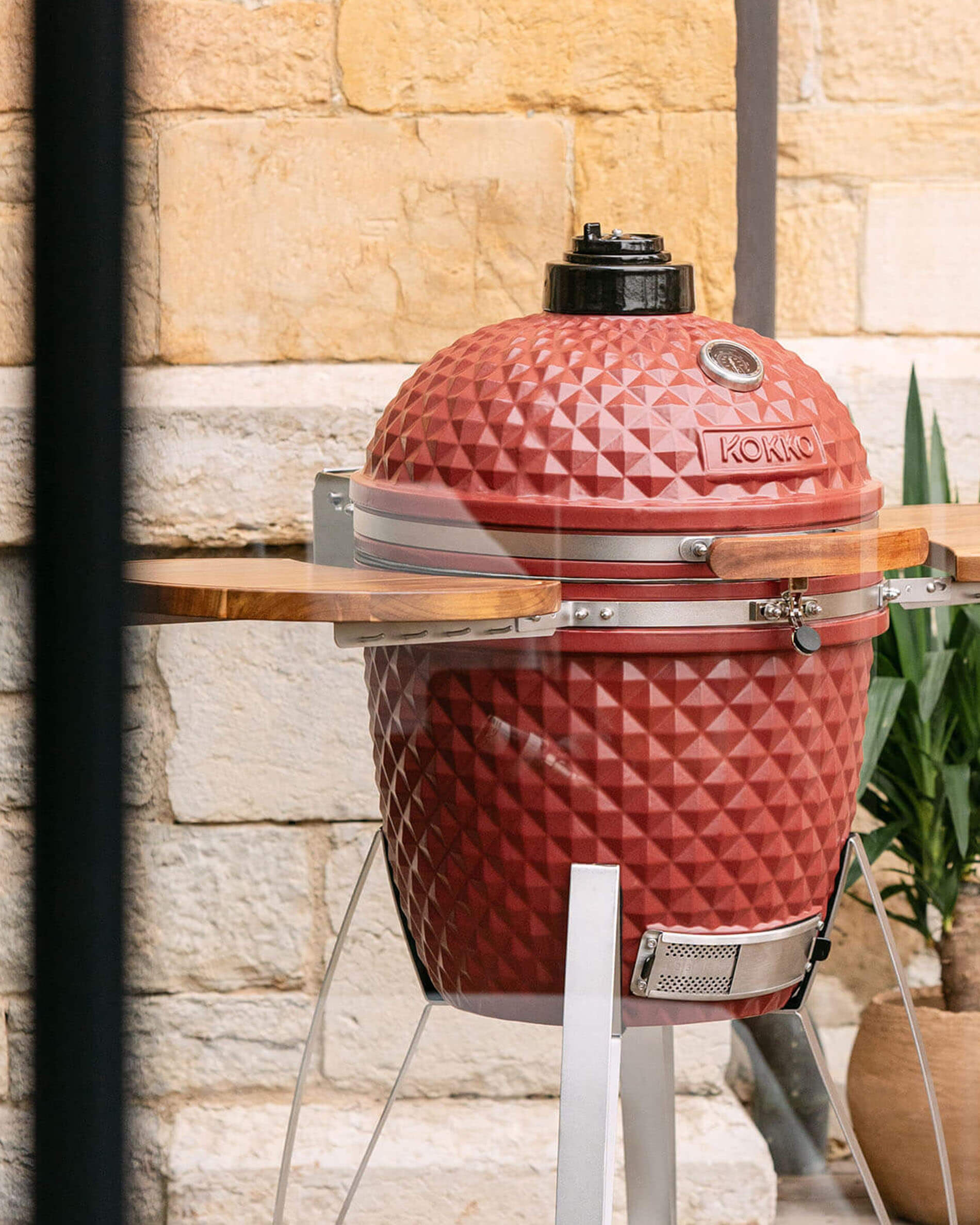 Kamado Kokko 22 polegadas em vermelho óxido, apresentado sozinho no exterior.