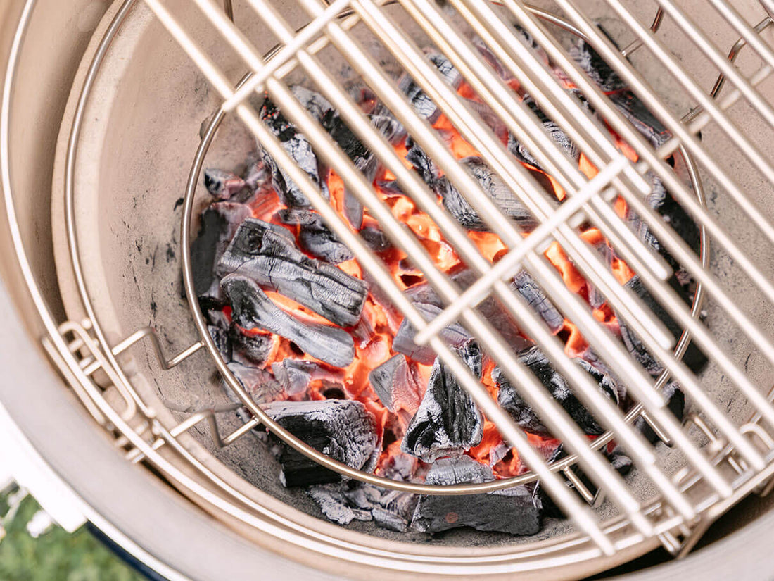 Carvão em brasa na cuba em cerâmica de um kamado Kokko, com brasas vermelhas visíveis sob a grelha em inox, ilustrando a subida de temperatura e o controlo preciso da cozedura a lenha.