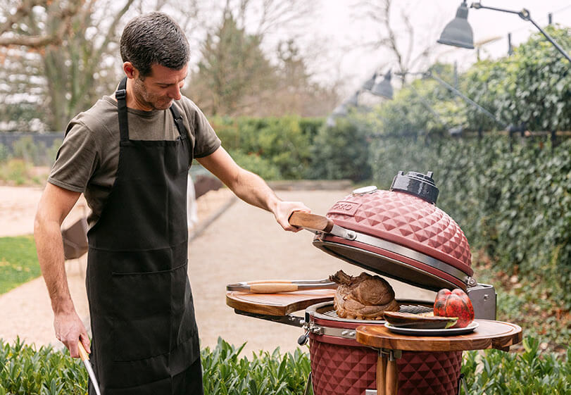Preparação de um assado num kamado Kokko vermelho, com a tampa aberta e manipulação dos alimentos no exterior.